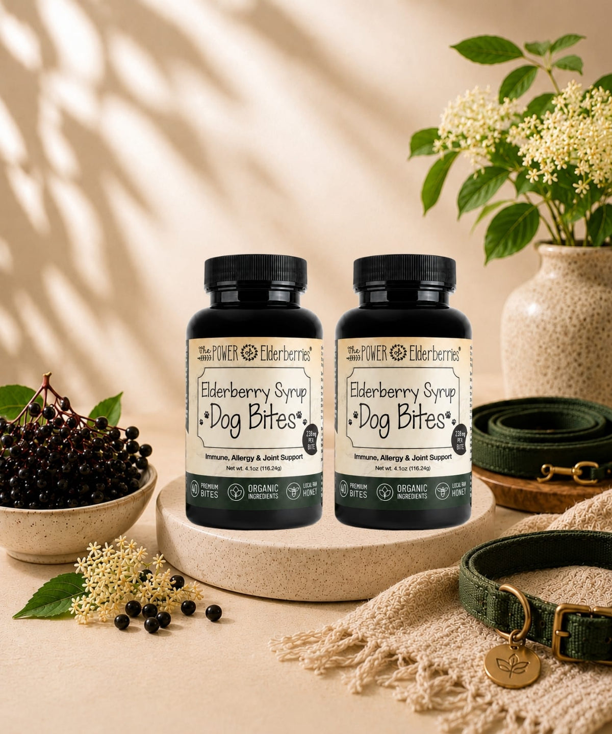Two bottles of Elderberry Syrup for Dog Bites on a beige surface with a vase of flowers and a bowl of berries in the background.