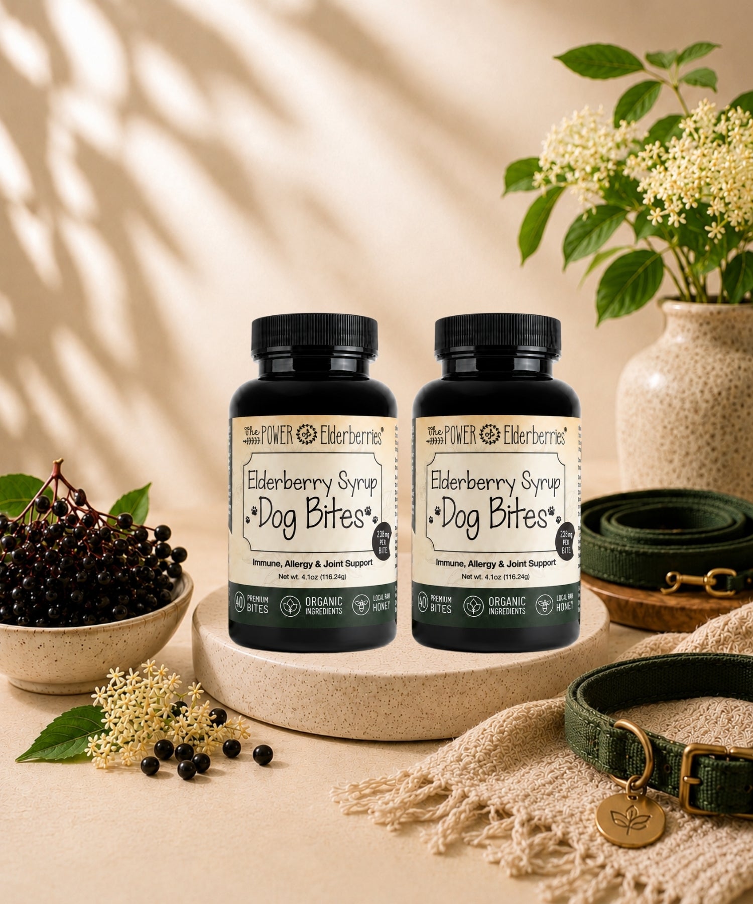Two bottles of Elderberry Syrup for Dog Bites on a beige surface with a vase of flowers and a bowl of berries in the background.