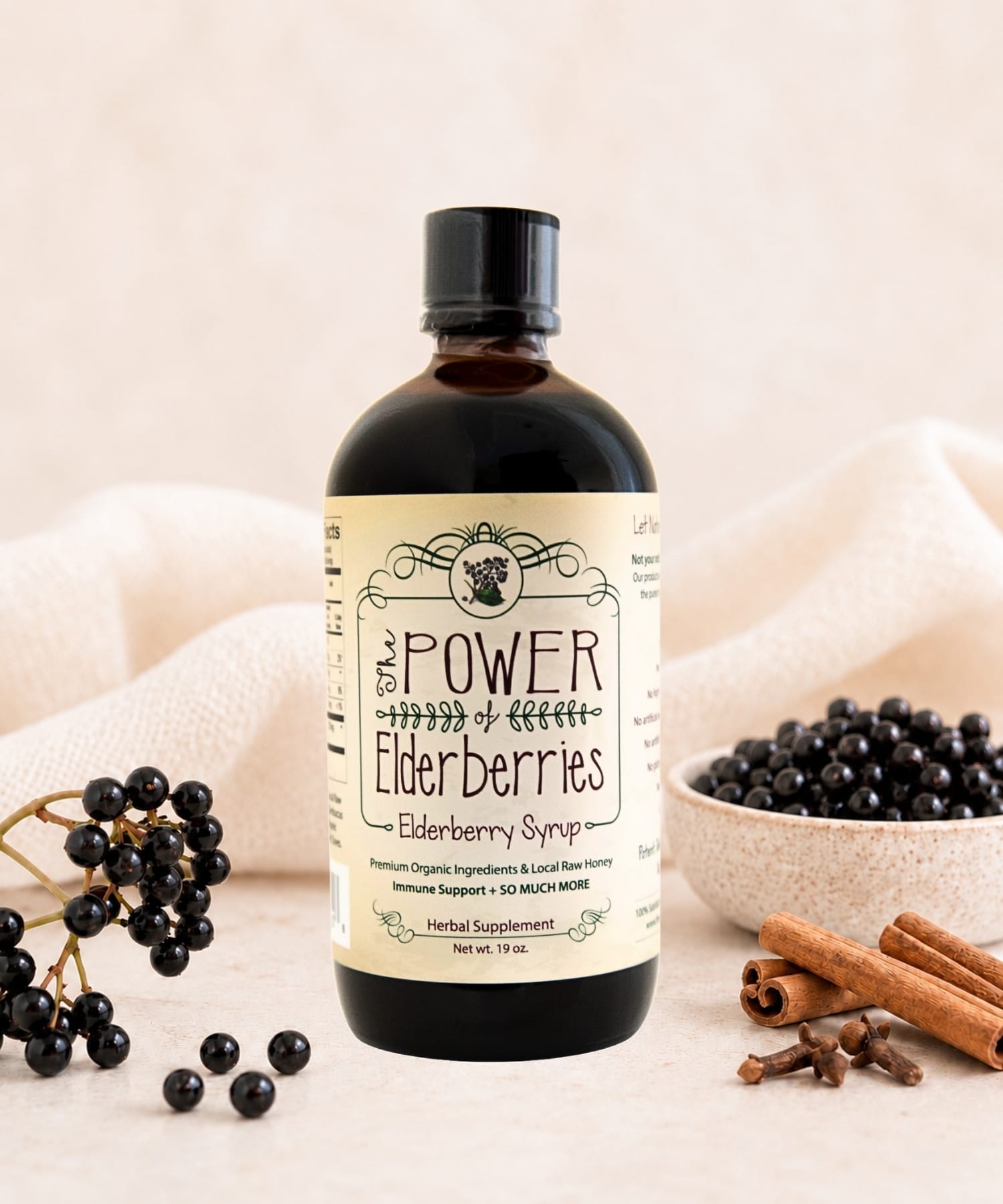 Fresh-made elderberry syrup sitting on the counter with organic black elderberries, cinnamon sticks, and whole cloves.