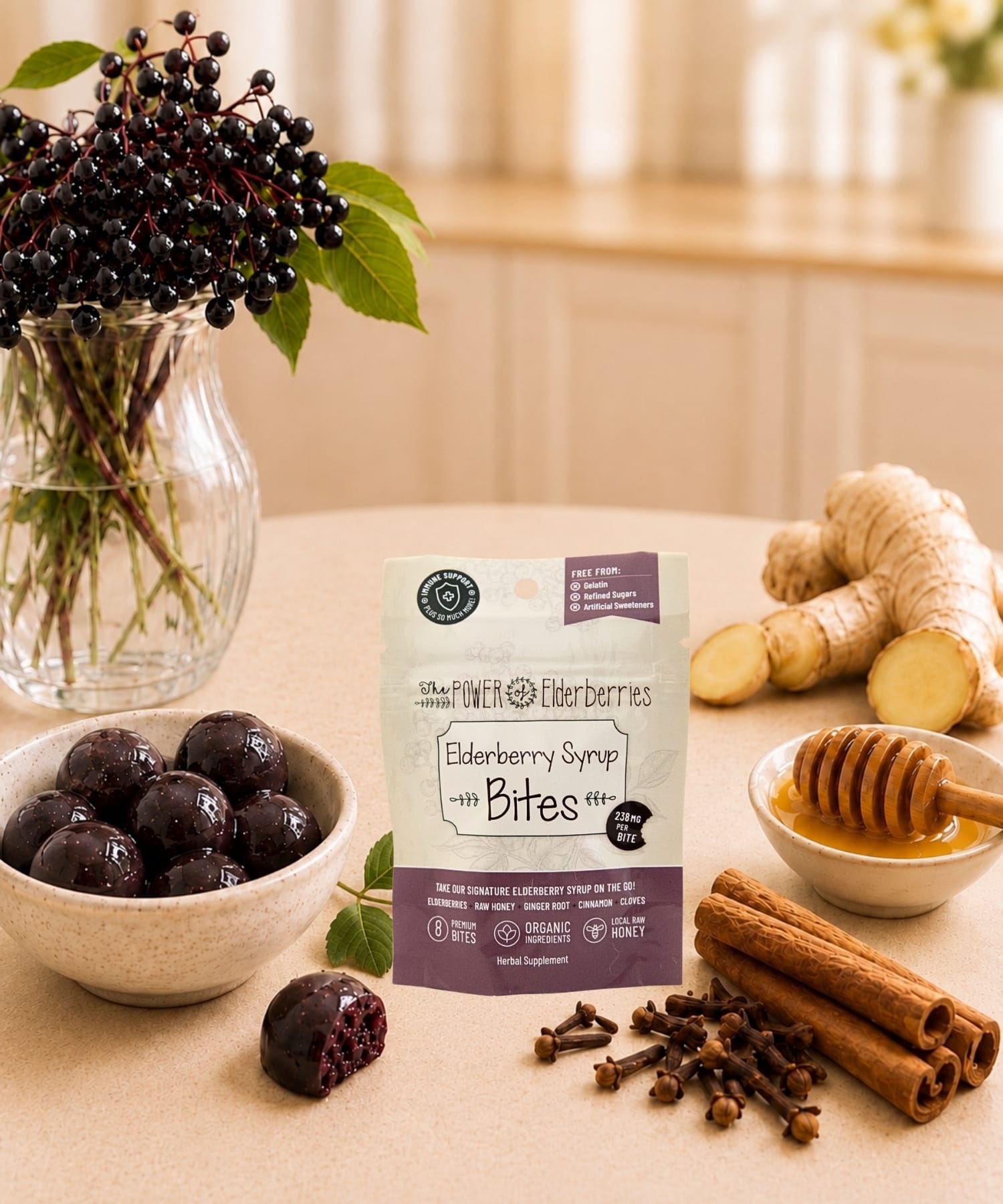 Elderberry syrup bites 8ct. pouch styled with elderberries, raw honey, ginger root, cinnamon sticks, and cloves on a warm countertop.