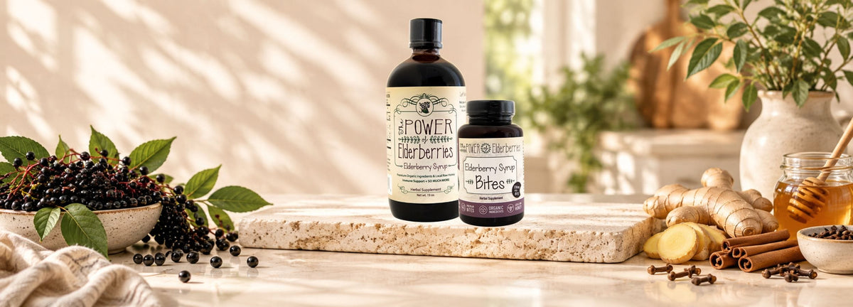 The POWER of Elderberries elderberry syrup and elderberry bites bottles, displayed on a stone slab with fresh berries, ginger, cinnamon, and honey in a warm, setting.